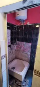 Niedokończony remont łazienki z odsłoniętymi przewodami hydraulicznymi i elektrycznymi, obok wanny otoczonej częściowo wyłożonymi kafelkami ścianami.