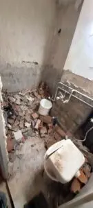 Zniszczona łazienka z połamanymi płytkami na podłodze, porozrzucanymi gruzami i wymagająca poważnego remontu.