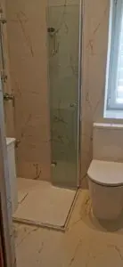 Nowoczesna łazienka z marmurowymi płytkami, wyposażona w przeszkloną kabinę prysznicową obok białej toalety.
